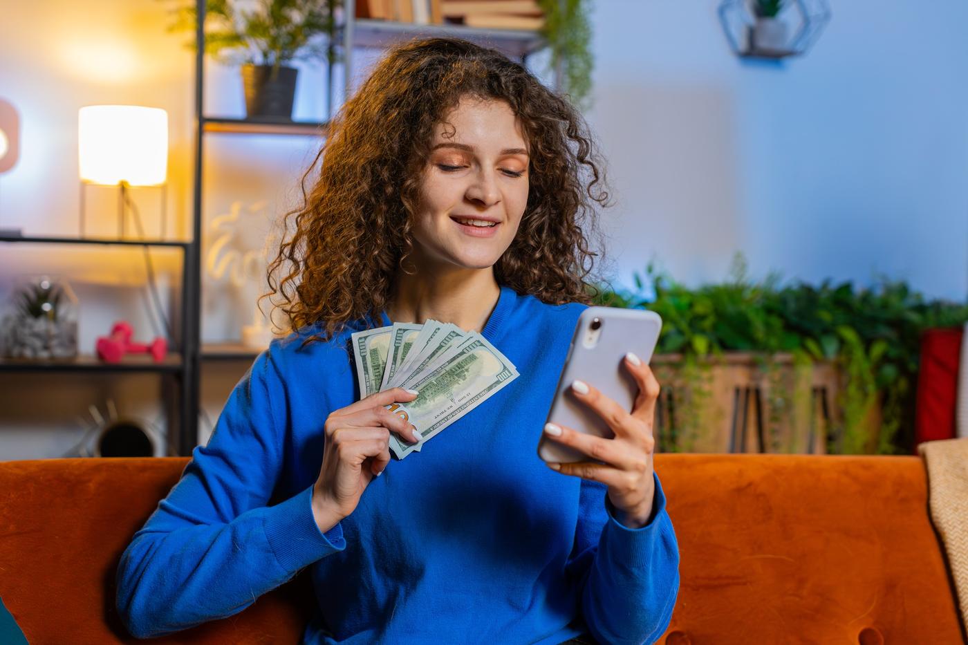 Mujer con billetes de dólares en la mano revisando el tipo de cambio en su celular